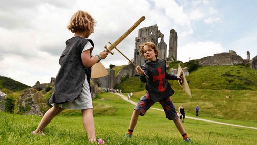 Two children play with toy swords in front of Corfe Castle in Dorset